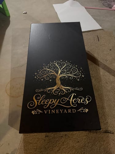 Customer's custom cornhole board wrap with an elegant gold tree and 'Sleepy Acres Vineyard' text on a black background.