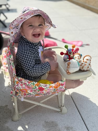Customer's happy baby sitting in the floral print Paloma portable booster chair outdoors.