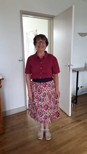 Une cliente porte la blouse Amandine bougainvillier, boutonnée et rentrée dans une jupe à motifs.