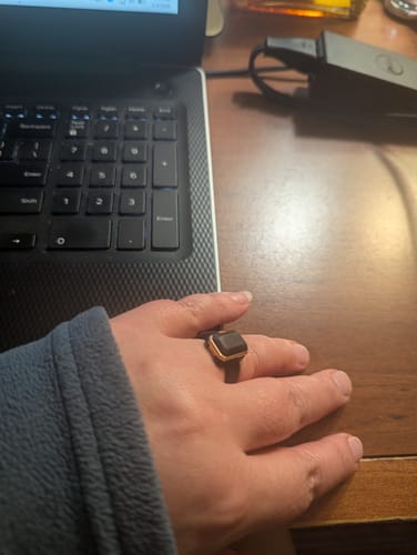A reviewer's hand on a desk, wearing the black Emerald Collection silicone ring with its gold-tone metal frame.