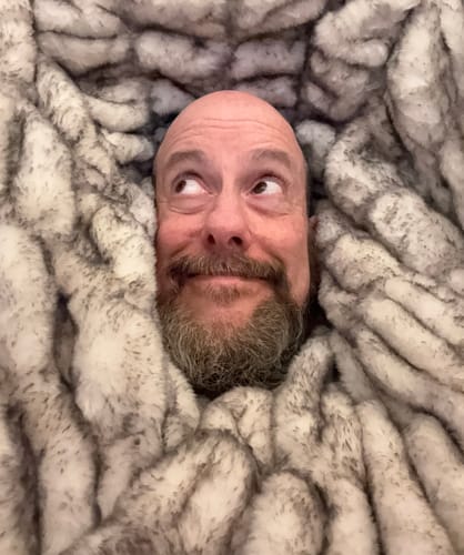 Reviewer playfully wrapped up in the soft, fluffy Hugs Obsidian Blanket, with only their head visible.