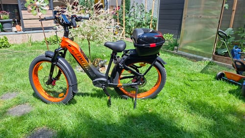 Reviewer's Lankeleisi MG600 Plus e-bike, with orange wheels and a rear storage box, parked on a green lawn.