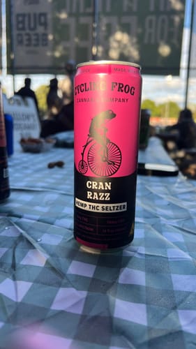 Customer's pink can of Cran Razz THC Seltzer from the Variety Pack, sitting on a checkered tablecloth outdoors.