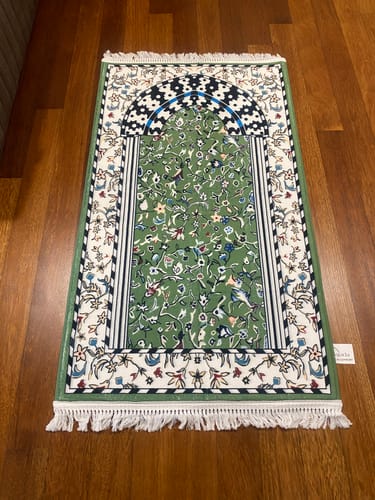 Customer's green Minbar Al Rawda Padded Prayer Mat with an intricate floral pattern laid flat on a wooden floor.