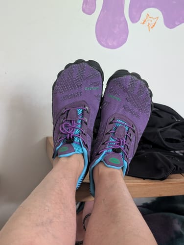 Customer's first-person view of their purple and blue Free I Barefoot Shoes on their feet.