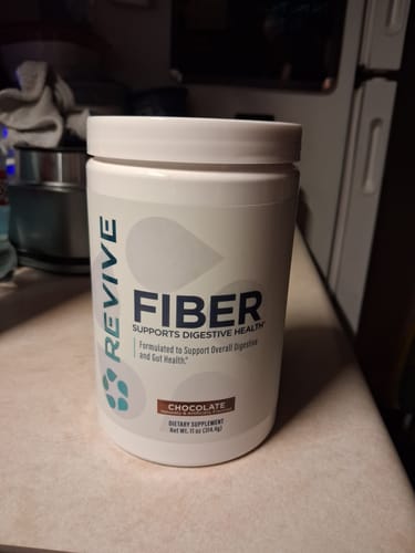 Customer's white tub of Revive Fiber digestive supplement, chocolate flavor, on a kitchen counter.