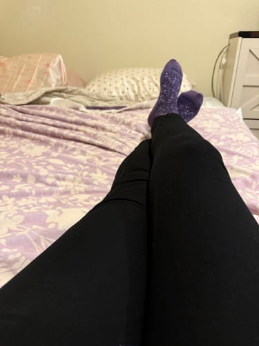 Customer's point of view, relaxing in bed with their legs under a purple floral blanket.