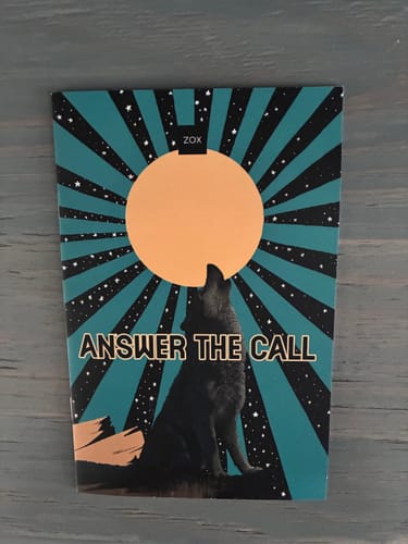Customer's July 2026 Booklet showing its graphic cover of a wolf howling at a large moon with text 'ANSWER THE CALL'.