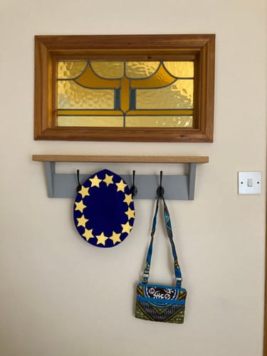 Customer's light grey coat rack with shelf mounted on a wall, holding a decorative item and a small bag.