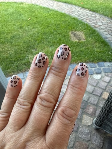 Hand einer Kundin mit den aufgetragenen UV-Gel-Nagelfolien 'Wild Elegance' mit feinem Leopardenmuster.