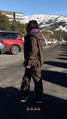 Reviewer from behind wearing the baggy coffee insulated snow pants in a snowy mountain parking lot.