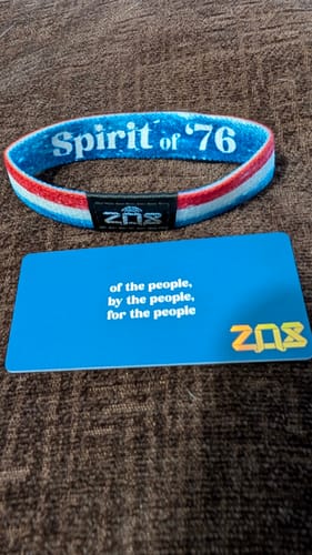 A customer's Spirit of '76 Bracelet, with red, white, and blue stripes, shown with its matching blue card on a brown surface.
