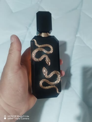 Un cliente sostiene el frasco de perfume Veneno, que es negro con un diseño de serpiente dorada en relieve.