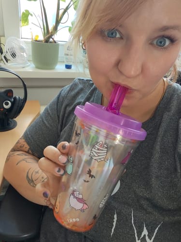 Eine Kundin trinkt aus dem Spooky Pusheen Becher mit lila Deckel und pinkem Strohhalm an ihrem Schreibtisch.
