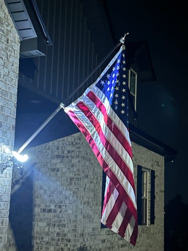 Reviewer's Prestige House Flag Pole with an American flag, mounted on a brick house and illuminated by a light at night.
