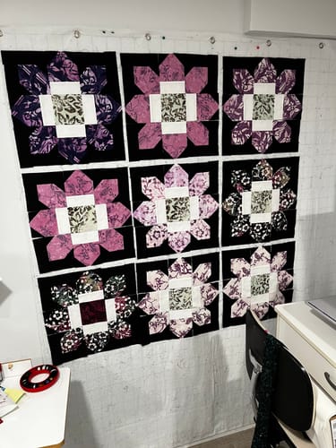 Customer's work-in-progress Edelweiss Quilt Kit, with nine assembled flower blocks pinned to a wall.