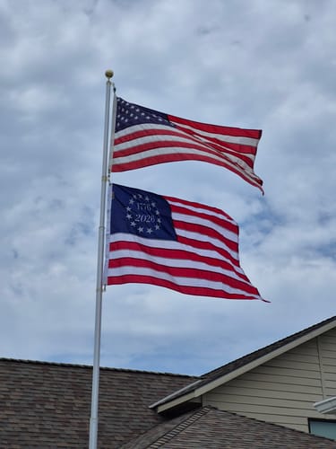 Customer's Betsy Ross Flag flying on a flagpole below a standard American flag against a cloudy sky.