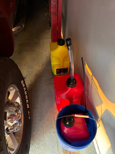 Customer's photo of various fuel cans and a bucket stored in a garage next to a tire.