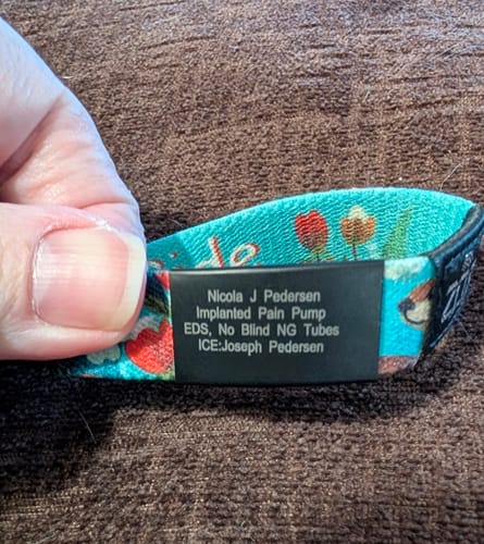 Close-up of a reviewer holding a colorful wristband with the black, engraved Medical Alert Bracelet Charm.