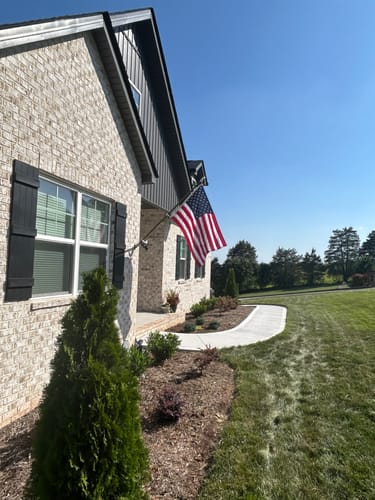Customer's Prestige House Flag Pole with American flag mounted to the front of a light brick house during the day.