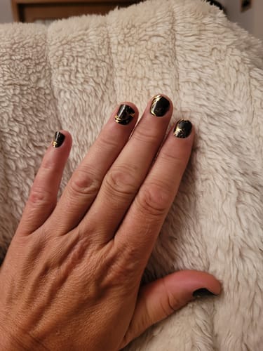 Hand einer Kundin, die die schwarzen und goldenen „Midnight Thoughts“ UV Gel-Folien nach 3 Wochen zeigt.