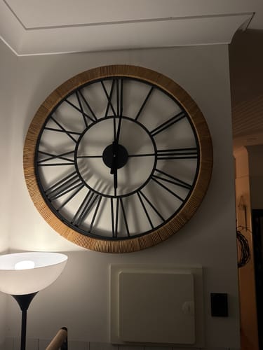 Customer's Hugo French Country Wall Clock mounted on a wall, showing the rattan frame and black Roman numerals.