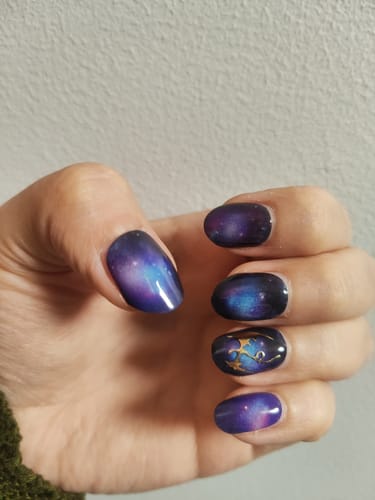 Hand einer Kundin, die die 'Moody Twilight' UV-Gel-Nagelfolien mit einem goldenen Nagelsticker auf dem Ringfinger trägt.