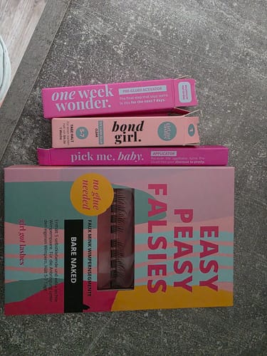 Ein Kunde zeigt die Verpackungen des Starter Sets Pre-Glued 2.0, mit BARE NAKED Wimpern, Aktivator und Applikator.
