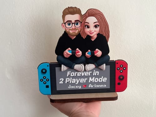 Customer holding a custom plaque of a couple on a gaming console, inscribed 'Forever in 2 Player Mode'.