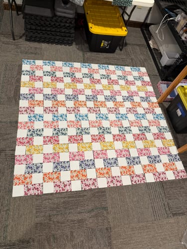 Customer's in-progress Brick Prairie Precut Quilt Kit top laid flat, showing the colorful floral brick and white square pattern.