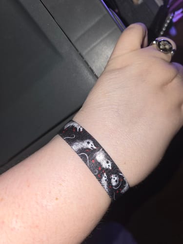 Close-up of a reviewer's wrist wearing the black I'd Play Dead For You Bracelet with a possum design.
