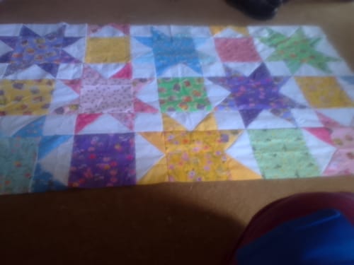 Reviewer's in-progress Cut Flowers Quilt top laid out, showing the colorful, patterned star block design.