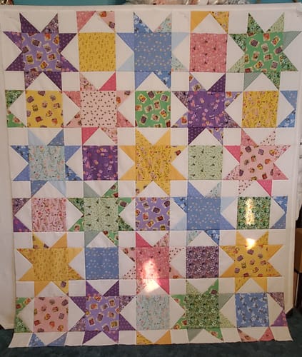 Reviewer's assembled Cut Flowers quilt top, showing bright, colorful star blocks made from the kit's patterned fabrics.
