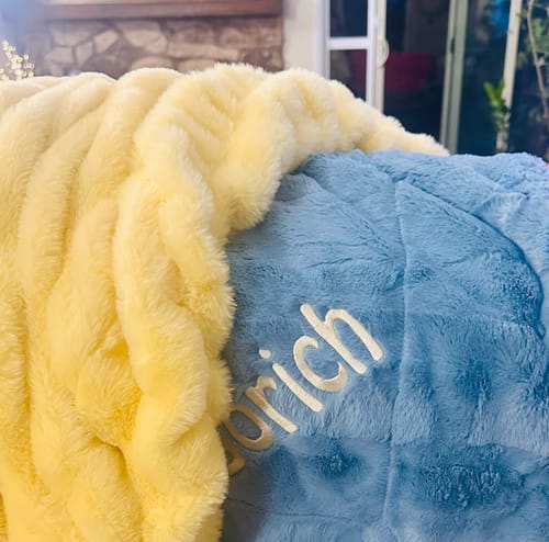 Customer's close-up of their plush Sorbet Denim Blanket with custom embroidery, shown next to a yellow blanket.