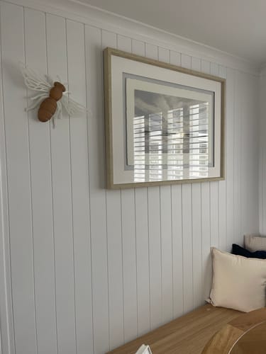 Customer photo of the Honey Bee wall decor on a white paneled wall, next to a framed artwork in a dining nook.
