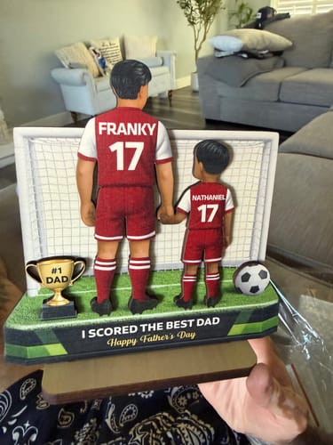 Customer holding a personalized soccer-themed keepsake showing two figures with the names 'Franky' and 'Nathaniel' on their jerseys.
