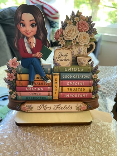 Customer's personalized wooden teacher plaque with a character sitting on books and the name 'Mrs Fields' on the base.