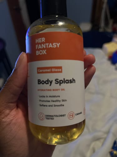 A customer holding the clear bottle of Caramel Glaze Body Splash body oil.