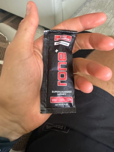 Reviewer holding a single packet of the Apple Cinnamon 100mg Caffeine SuperCharged Honey.