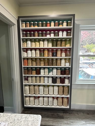 Reviewer's large pantry rack showcasing dozens of mason jars filled with food, sealed with the Mason Genie Vacuum Sealer Kit.
