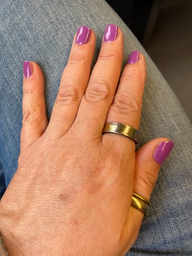 Nahaufnahme der Hand einer Kundin mit den glänzenden, violetten UV-Gel-Nagelfolien 'Sugarplum Song' auf den Nägeln.