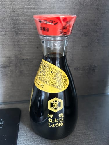 Customer's traditional glass bottle of Kikkoman Shoyu Soy Sauce, sealed and sitting on a counter.