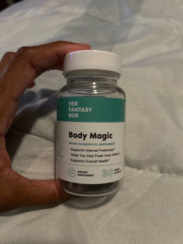 Reviewer's hand holding a clear bottle of Body Magic Chlorophyll Pills, showing the capsules inside.