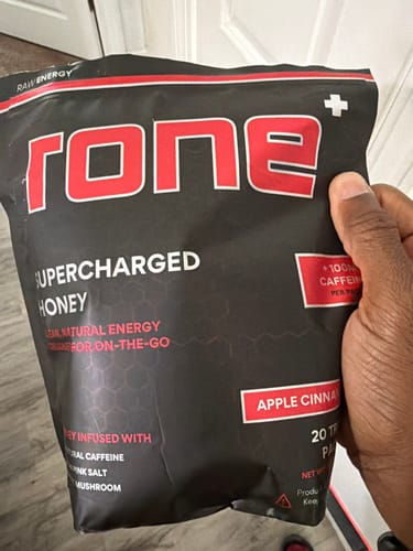 Customer's hand holding a large black bag of rone+ SuperCharged Honey in the Apple Cinnamon flavor.