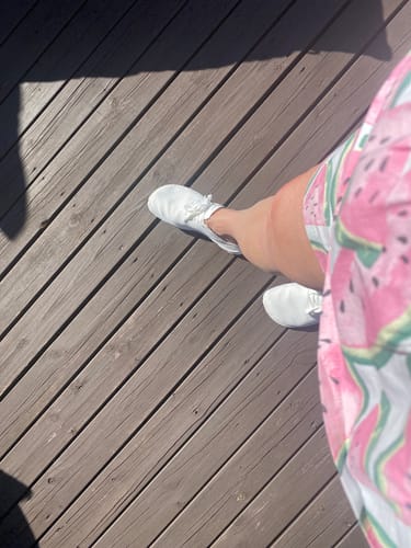 Arvostelijan jalassa valkoiset Vaistoa Iloa -paljasjalkatennarit puisella terassilla.