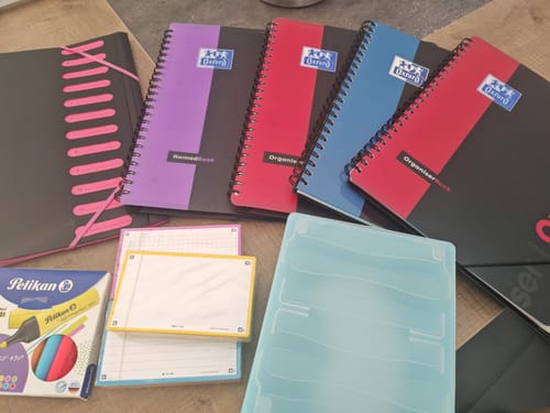 Client montrant plusieurs cahiers à spirales ORGANISER BOOK OXFORD colorés sur une table avec d'autres fournitures.