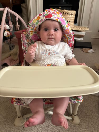 Reviewer's baby sitting in the Paloma baby chair with a matching floral hat and attached tray.