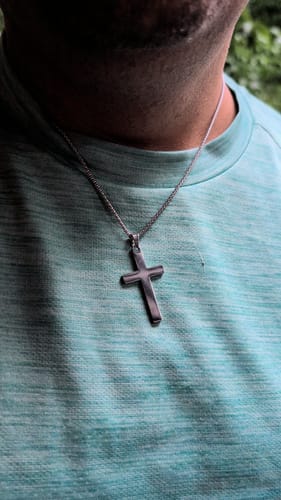 Customer wearing The Apostle Cross, a polished silver necklace, against a teal t-shirt.