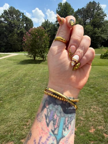 Customer wearing the gold Marbella Cuff Bracelet layered with a beaded bracelet on their tattooed wrist.