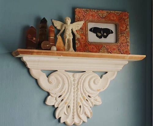 A customer displays crystals and art on their white, carved Virginie Mantel Shelf, mounted on a blue wall.